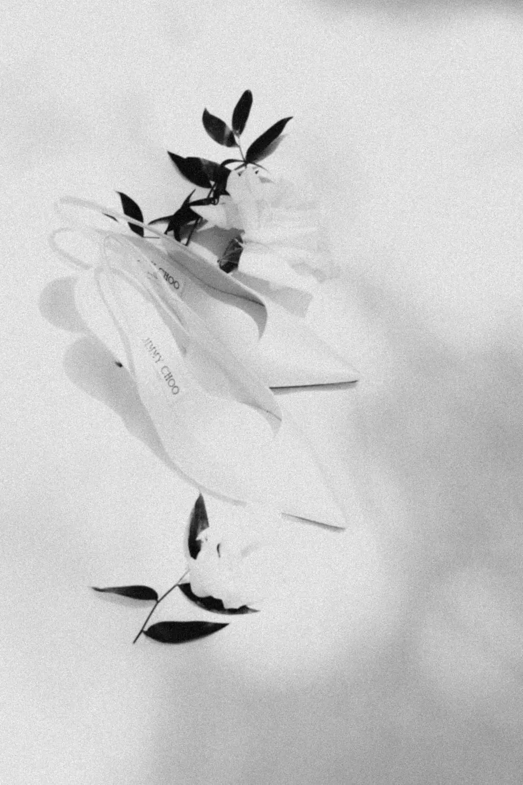 White Jimmy Choo bridal heels arranged with jasmine sprigs on soft fabric, photographed in grainy black and white.