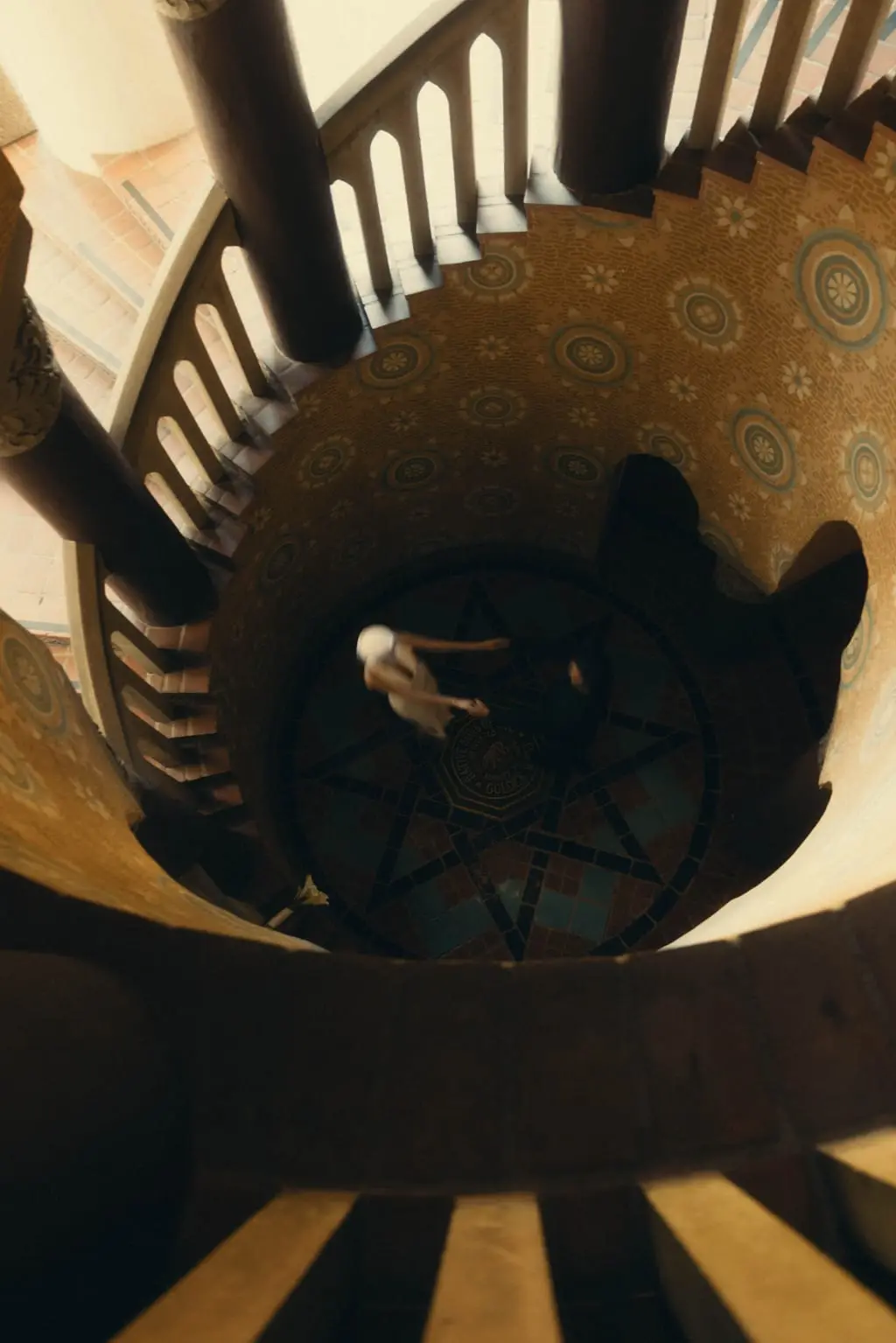 Overhead view down a tiled spiral staircase onto a mosaic star floor where the bride and groom dance together inside a Spanish colonial landmark.