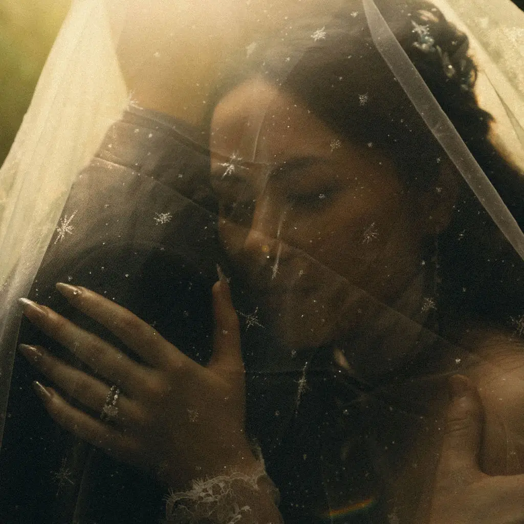 Bride with closed eyes rests beneath a star-embroidered veil showing her ring in golden light